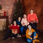 A family posing with Christmas gifts by a decorated tree indoors, exuding holiday warmth.