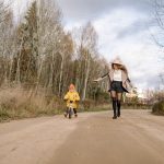 Woman and child on a dirt road in autumn forest, enjoying outdoor fun and nature.